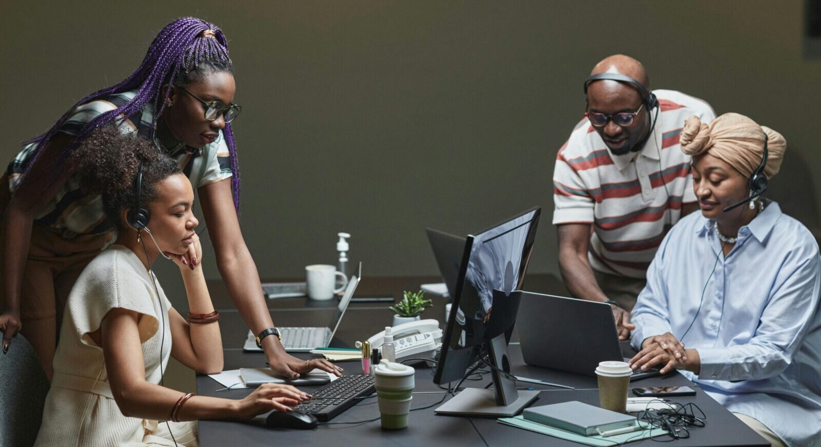 A diverse team of professionals collaborating in a modern office environment, using headsets and computers.