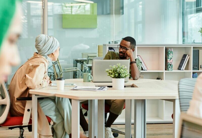 Diverse team collaborating in a modern office, engaging in conversation around desks.